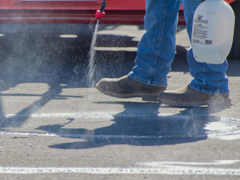 A closeup of a person spraying liquid from a hand sprayer onto a paved surface.
